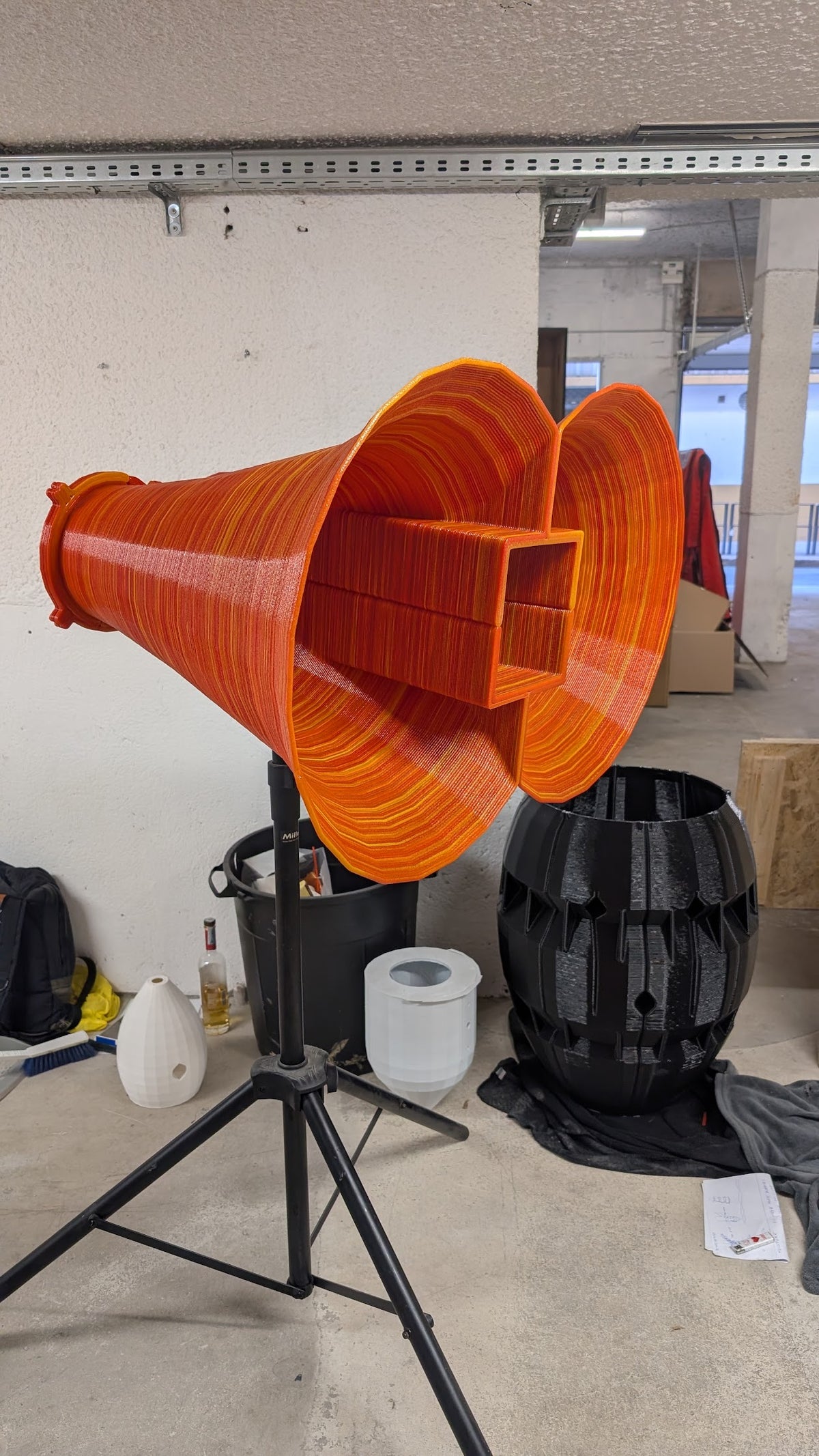 Corneta acustica laranja impressa em 3D sobre tripe, ao lado de peca preta impressa